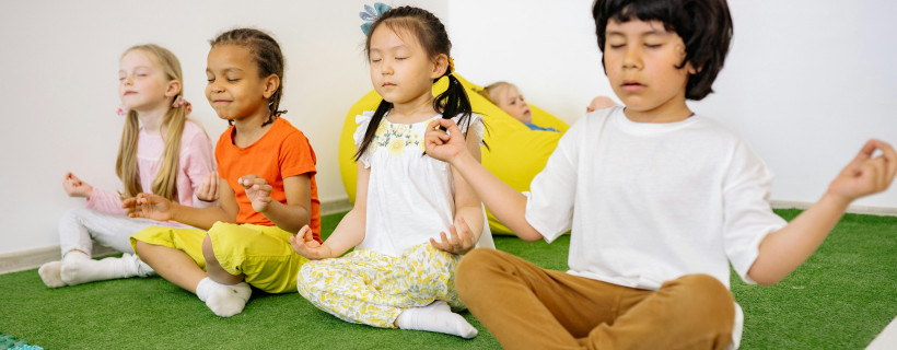 vier Kinder sitzen im Schneidersitz und meditieren